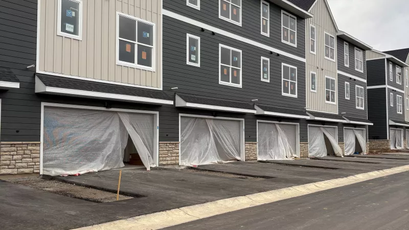 Three-story townhome buildings with gray and beige siding, covered garage openings, and new pavement throughout the developing apartment community.