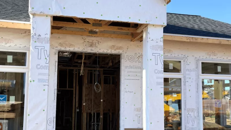 Close-up of a townhome entrance under construction, featuring Tyvek weather-resistive barrier and framed columns flanking the doorway.