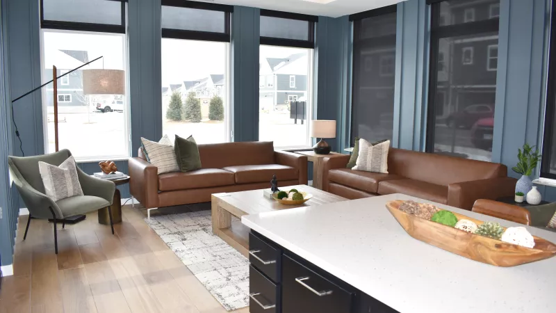 Spacious modern living room with blue walls, large windows, two brown leather sofas, a green armchair, and a kitchen island.