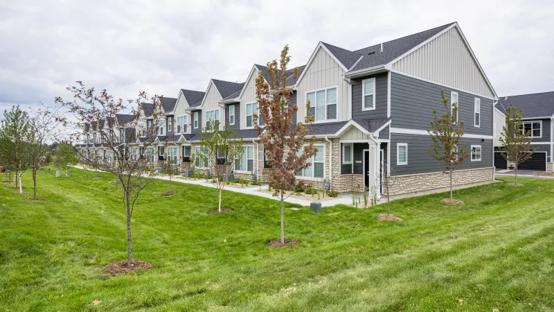 Row of modern townhouses with dark gray siding, light gables, and stone accents, set against a green lawn and cloudy sky.