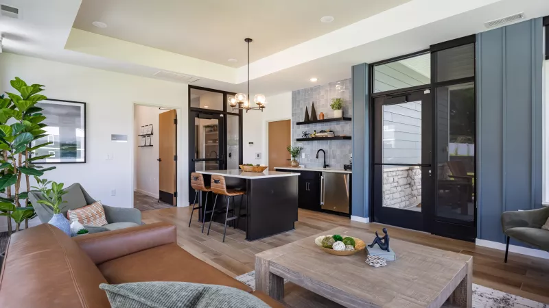 Stylish open-concept living space with a brown sofa, wood coffee table, and a modern kitchen island with dark cabinetry. Light wood floor.