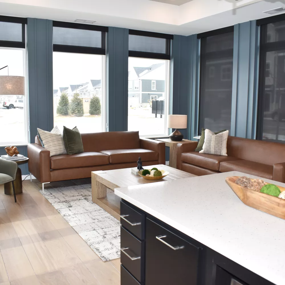 Spacious modern living room with blue walls, large windows, two brown leather sofas, a green armchair, and a kitchen island.