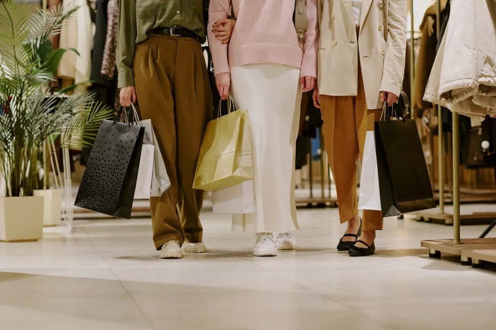Three people, from the waist down, walk through a clothing store carrying shopping bags.