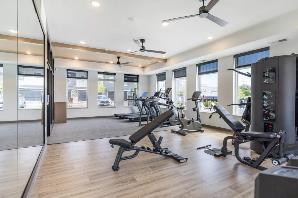 Bright gym with a weight bench, treadmills, exercise bikes, and a large mirror.